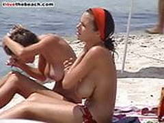 2 busty young girls oil their boobs on the beach